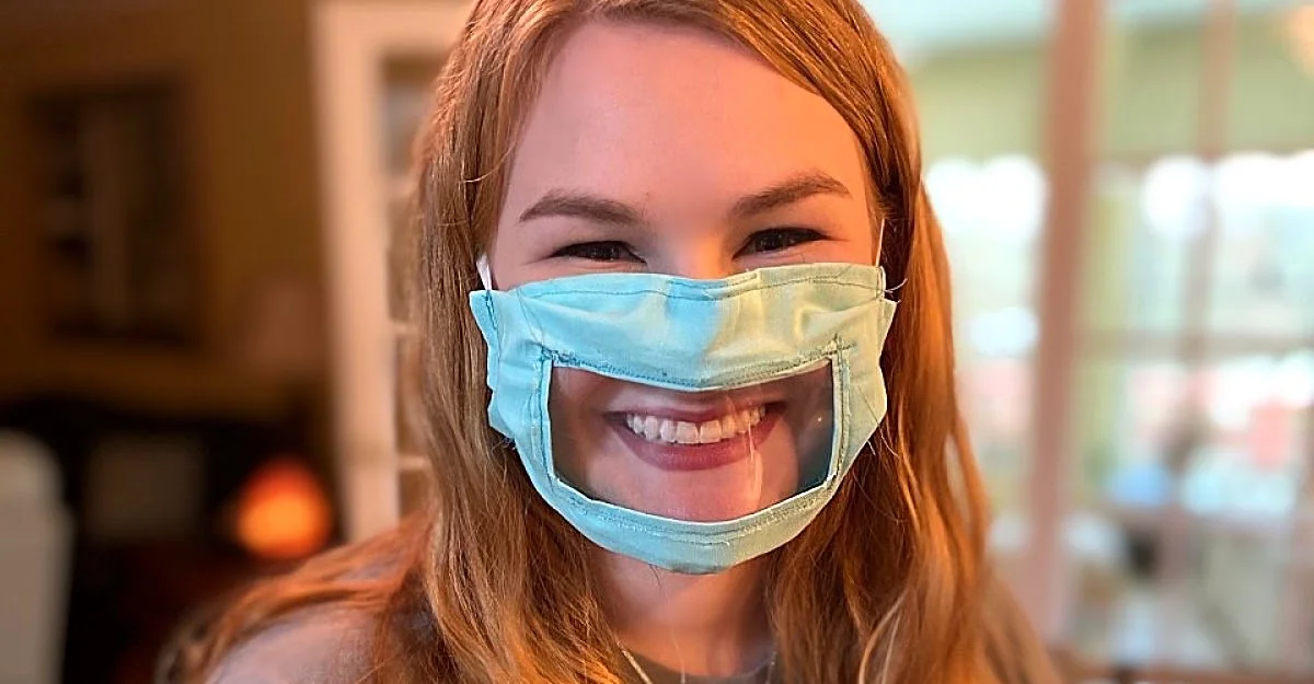 Jovem sorrindo com máscara transparente na região na boca.